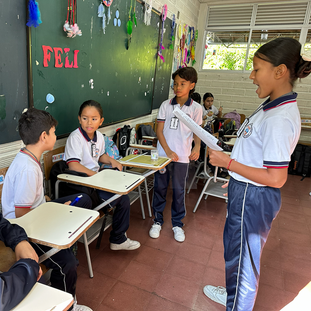 Trabajo en equipo de estudiantes de primaria distribuyendo tareas y recursos para un proyecto interactivo.