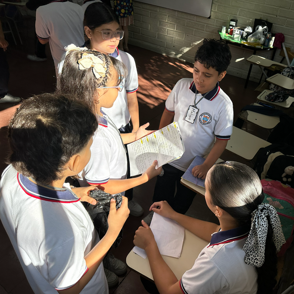 Trabajo en equipo de estudiantes de primaria distribuyendo tareas y recursos para un proyecto interactivo.
